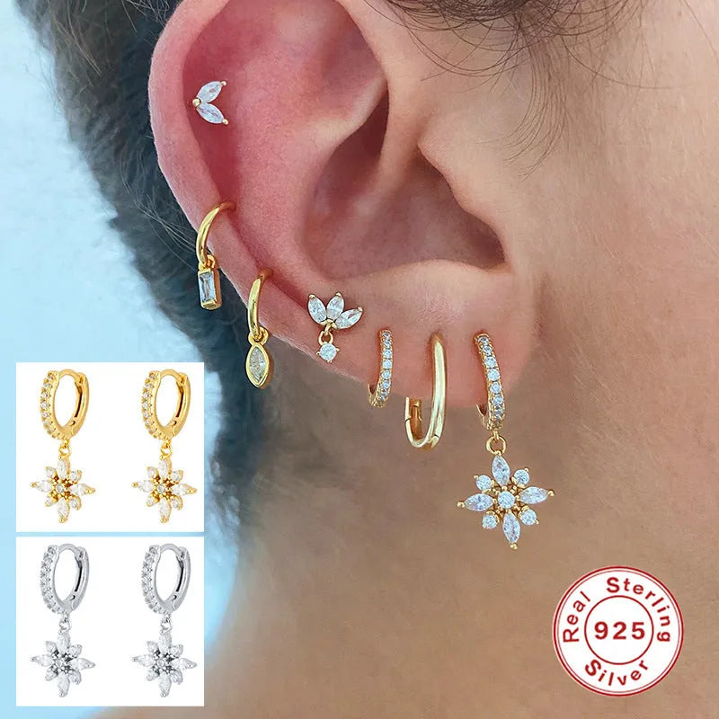 A pair of geometric snowflake pendant earrings in sterling silver with cubic zirconia stones, on a white background.