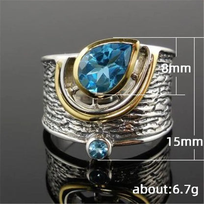 Close-up of a women's blue zircon ring with a teardrop-shaped stone inlaid in an alloy band, shown on a finger.