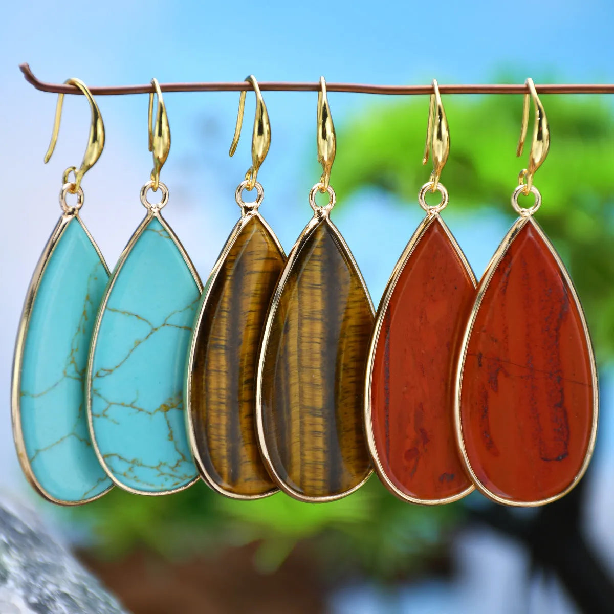 Handmade vintage long water drop earrings with tigereye stone and sterling silver hooks on a textured background.