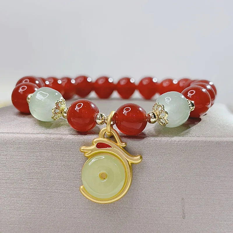 Close-up of a red agate bracelet with a dragon charm and Lucky Bag symbol on a wrist.
