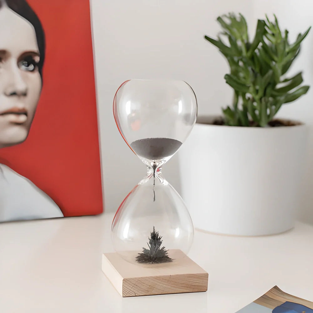 Captivating magnetic hourglass with a solid wood base and glass chamber, creating a mesmerizing display of temporary stalagmites.