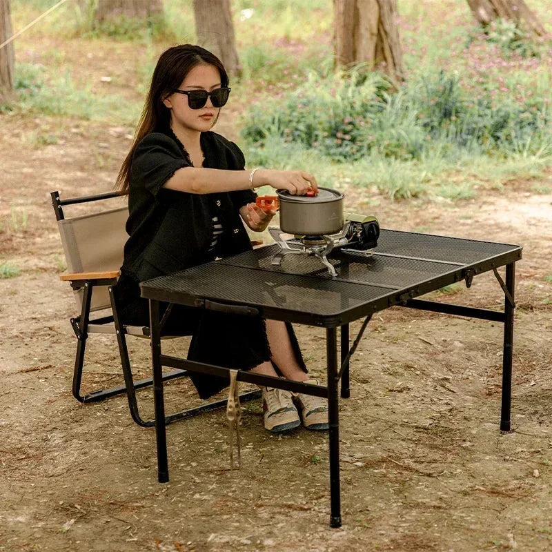 Adjustable portable folding camping table with aluminium frame, black in colour, set up outdoors