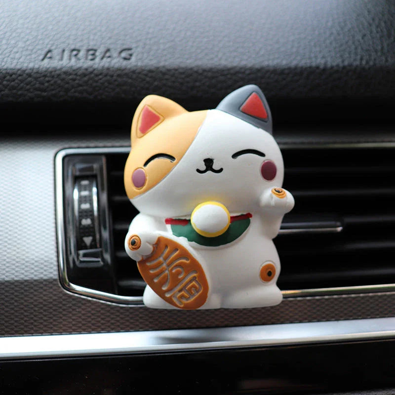 A black resin lucky cat car air freshener clipped onto a car vent, providing a refreshing fragrance and whimsical charm.