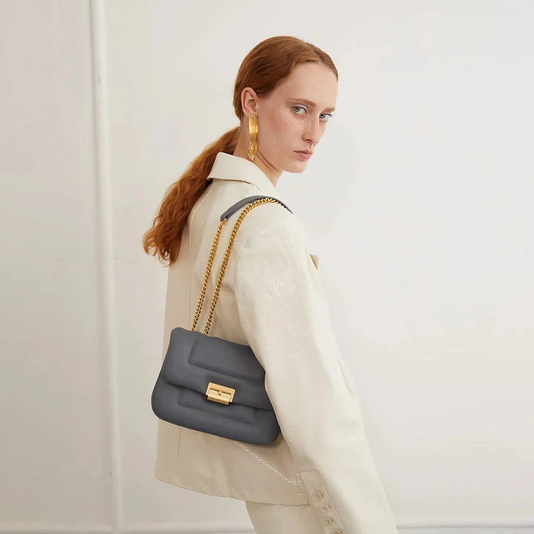 Grey leather crossbody bag with adjustable metal shoulder strap and secure hasp closure