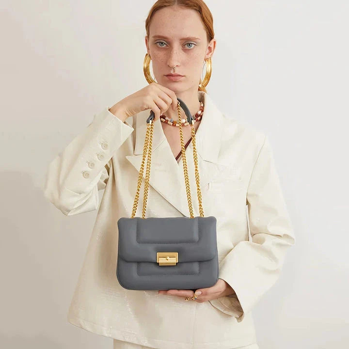 Grey leather crossbody bag with adjustable metal shoulder strap and secure hasp closure