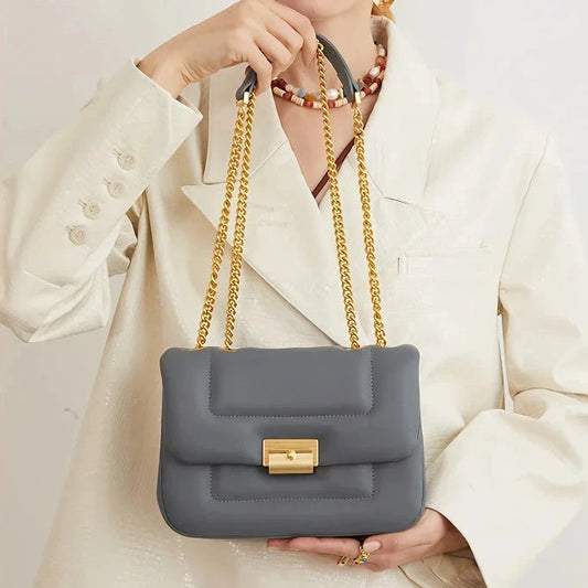Grey leather crossbody bag with adjustable metal shoulder strap and secure hasp closure