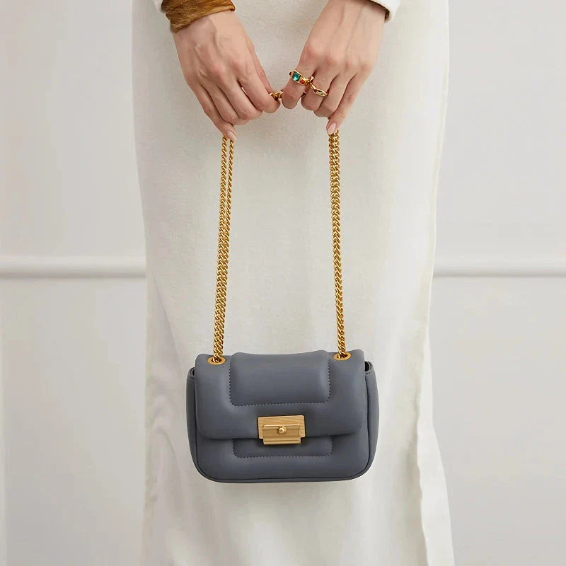 Grey leather crossbody bag with adjustable metal shoulder strap and secure hasp closure