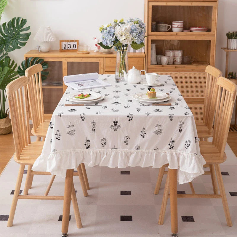 A high-quality cotton tablecloth with elegant floral embroidery and ruffled edges, creating a refined and charming dining experience.