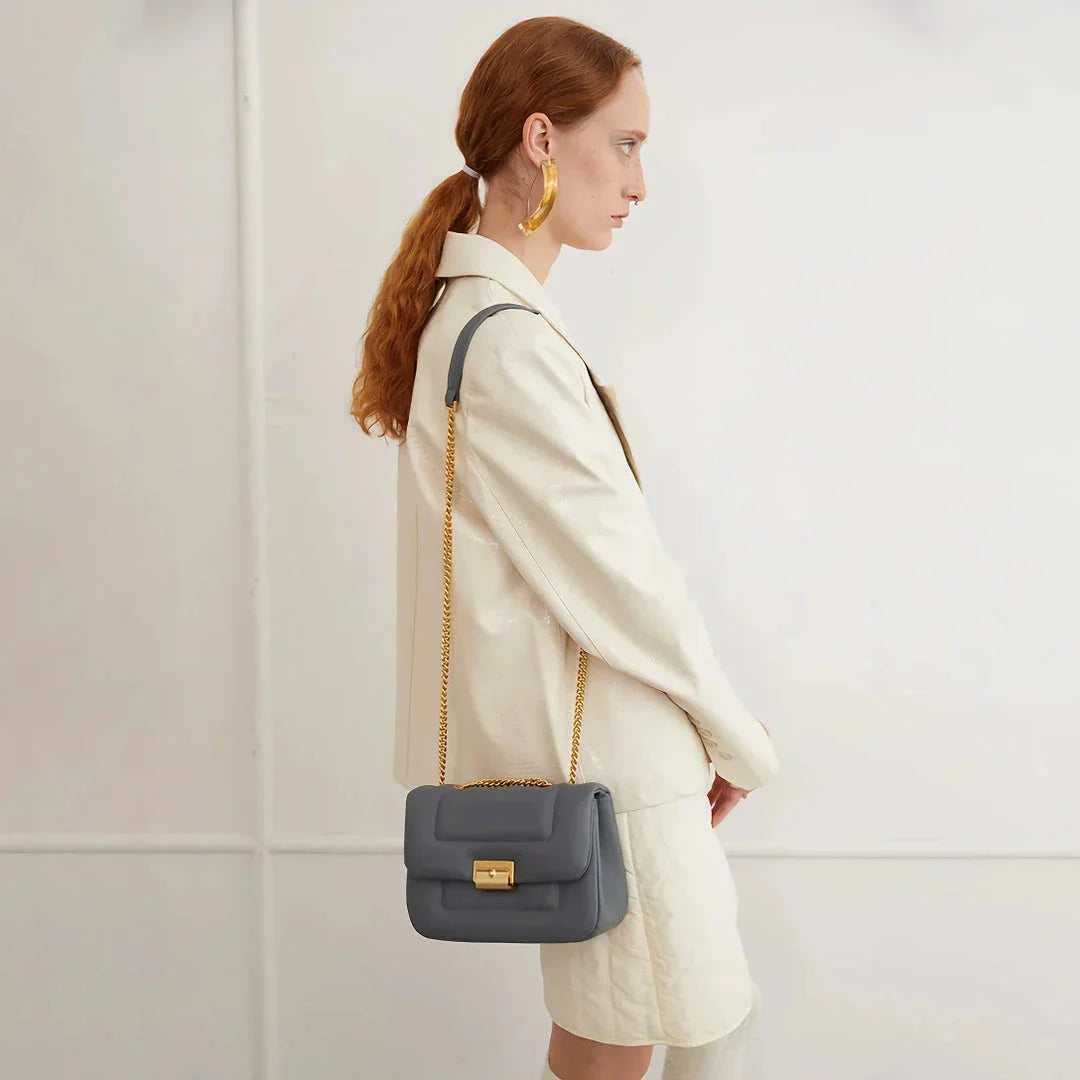 Grey leather crossbody bag with adjustable metal shoulder strap and secure hasp closure