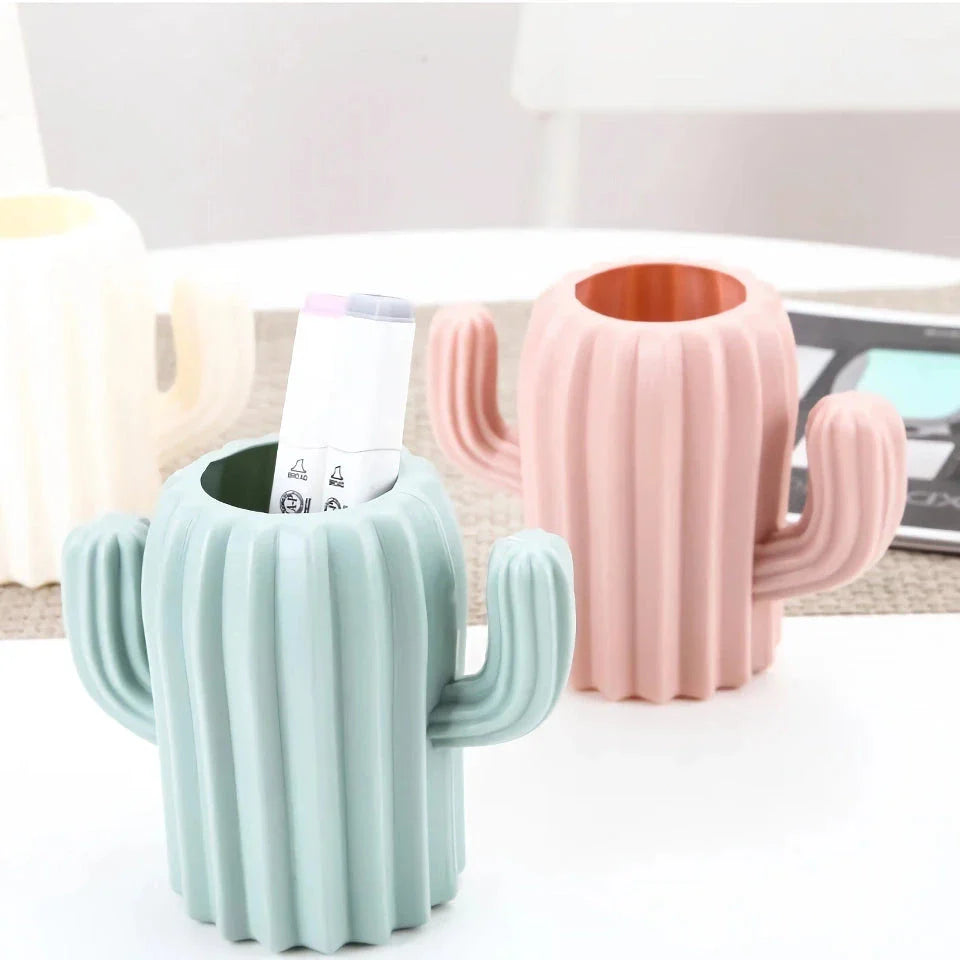 A white cactus-shaped desktop organiser holding pens, pencils, and makeup brushes on a wooden desk