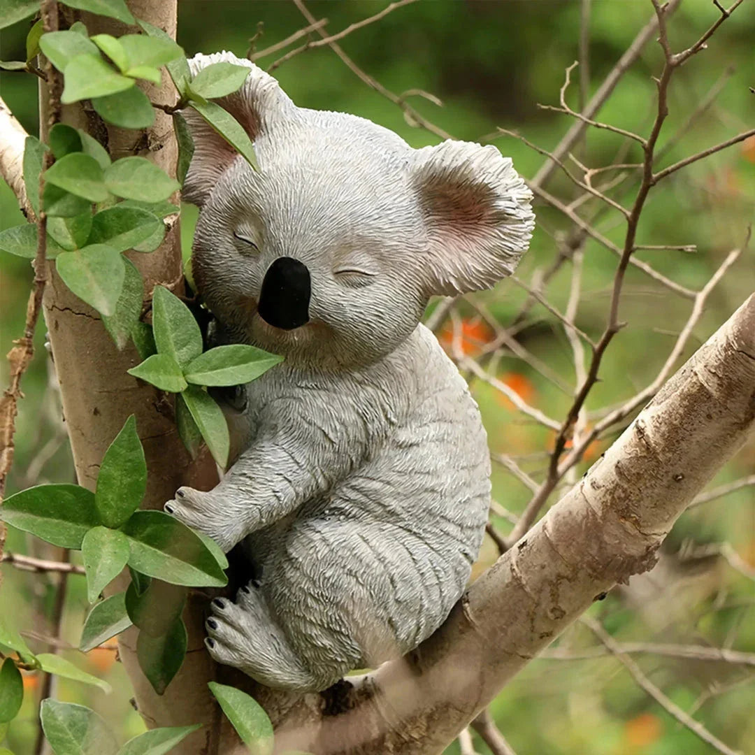 A lifelike grey resin koala statue climbing on a tree, adding a charming and whimsical touch to a garden or outdoor space