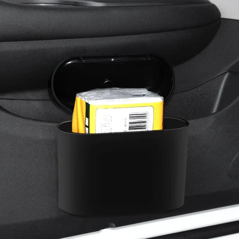 A compact black car bin with a press-type lid, designed to hang on the door panel and store garbage securely