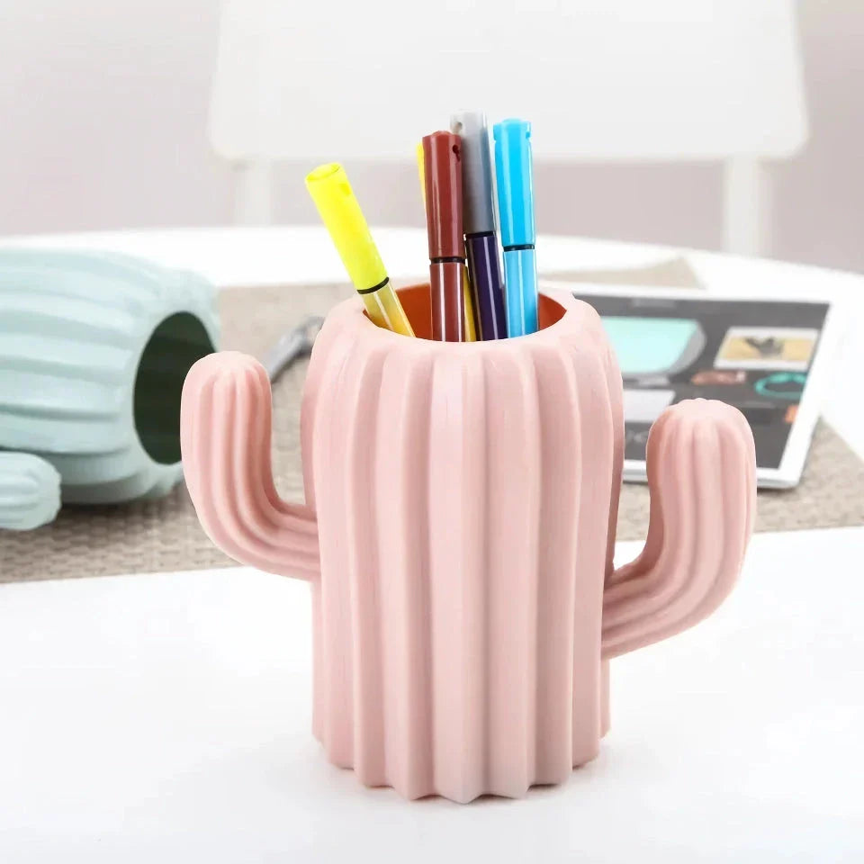 A white cactus-shaped desktop organiser holding pens, pencils, and makeup brushes on a wooden desk