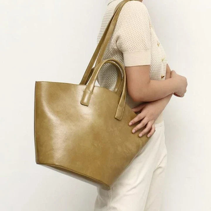 Elegant vegan leather tote bag with a unique bucket shape, short handles, and long straps for versatile carrying options
