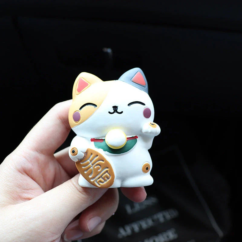 A black resin lucky cat car air freshener clipped onto a car vent, providing a refreshing fragrance and whimsical charm.