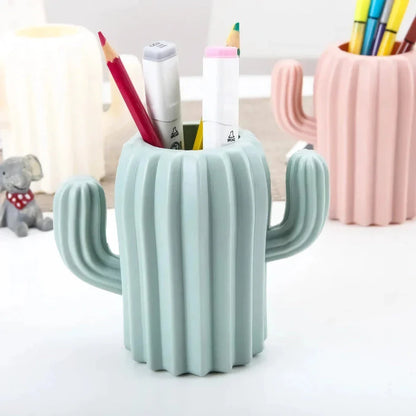 A white cactus-shaped desktop organiser holding pens, pencils, and makeup brushes on a wooden desk