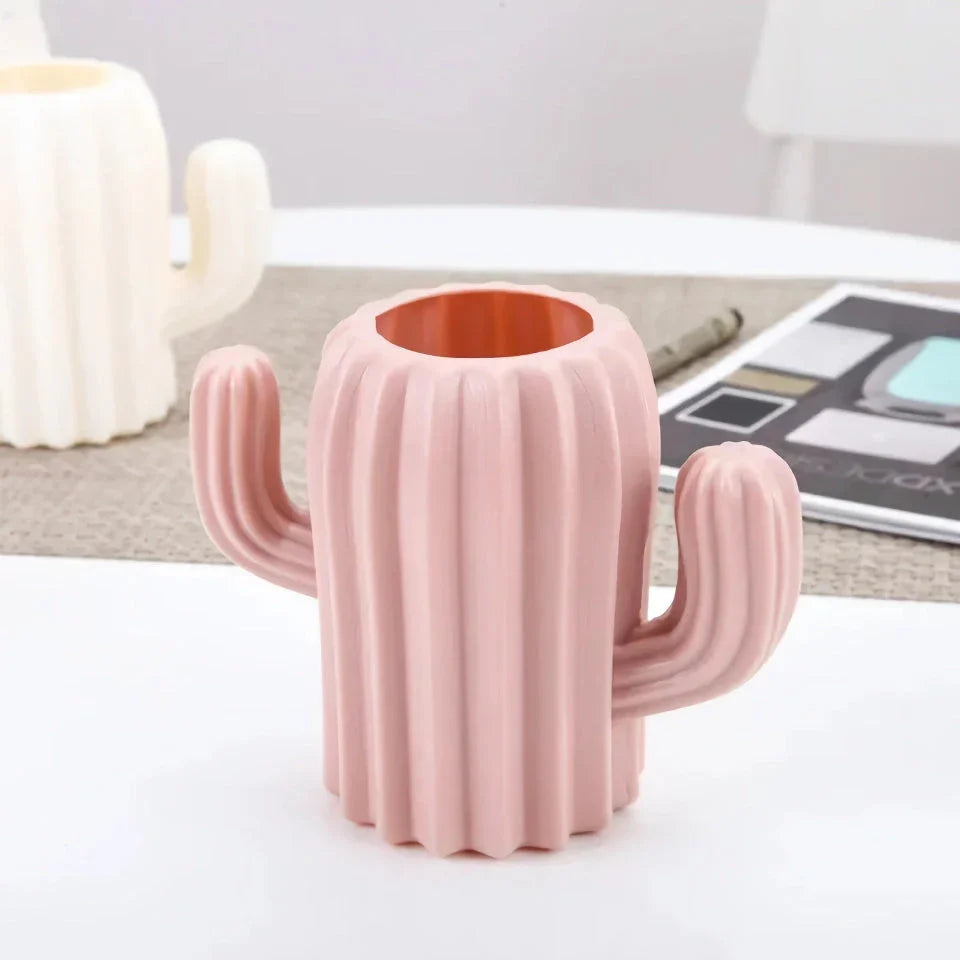 A white cactus-shaped desktop organiser holding pens, pencils, and makeup brushes on a wooden desk