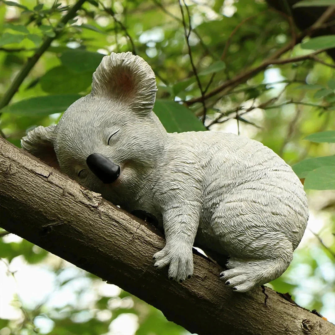 A lifelike grey resin koala statue climbing on a tree, adding a charming and whimsical touch to a garden or outdoor space