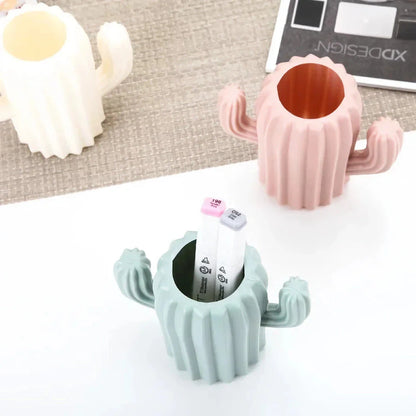 A white cactus-shaped desktop organiser holding pens, pencils, and makeup brushes on a wooden desk