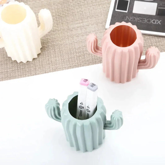 A white cactus-shaped desktop organiser holding pens, pencils, and makeup brushes on a wooden desk
