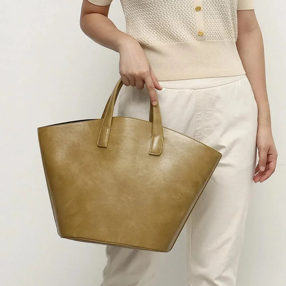 Elegant vegan leather tote bag with a unique bucket shape, short handles, and long straps for versatile carrying options