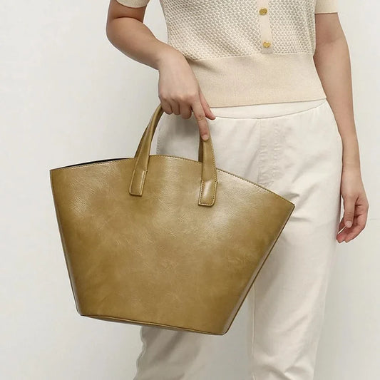 Elegant vegan leather tote bag with a unique bucket shape, short handles, and long straps for versatile carrying options