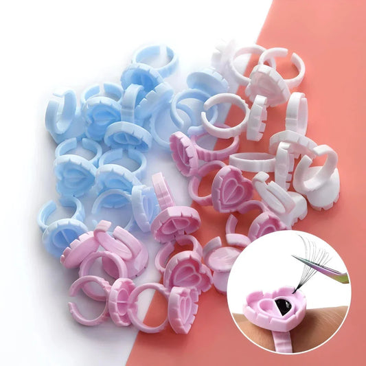 Heart-shaped disposable eyelash glue rings in blue, pink, and white colours for professional and at-home eyelash extension use